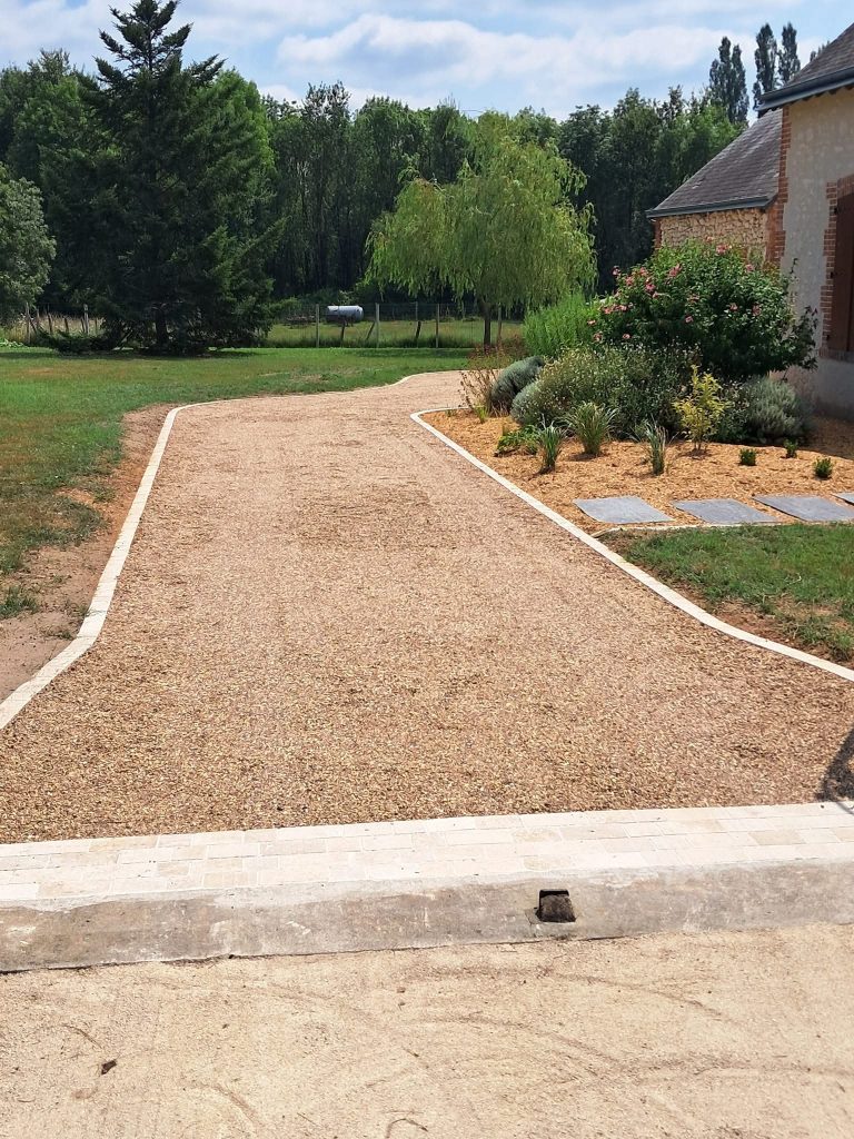 allée en gravillons beige qui mène à une habitation. Pelouse verte tondue dans le fond