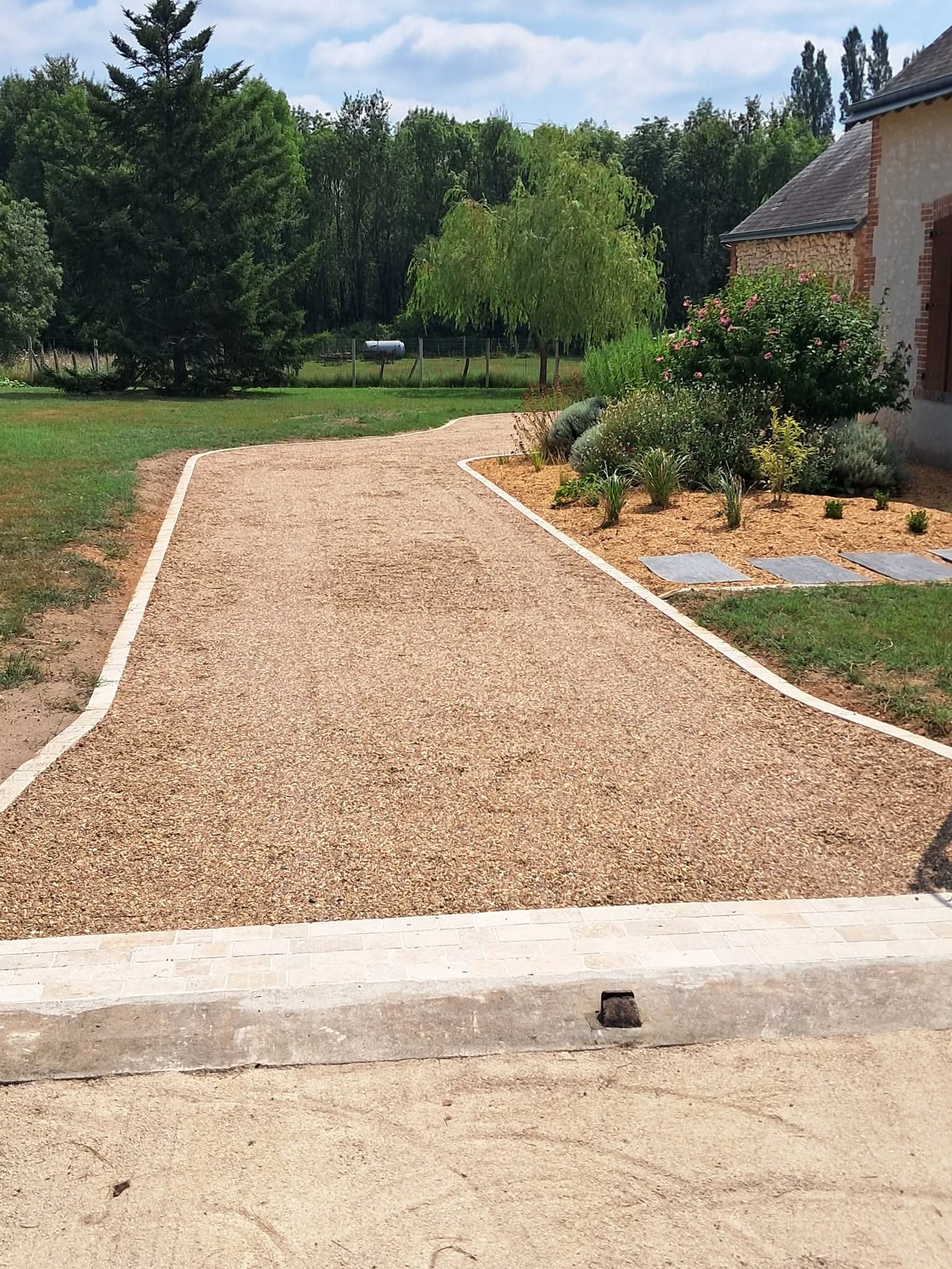 allée en gravillons beige qui mène à une habitation. Pelouse verte tondue dans le fond