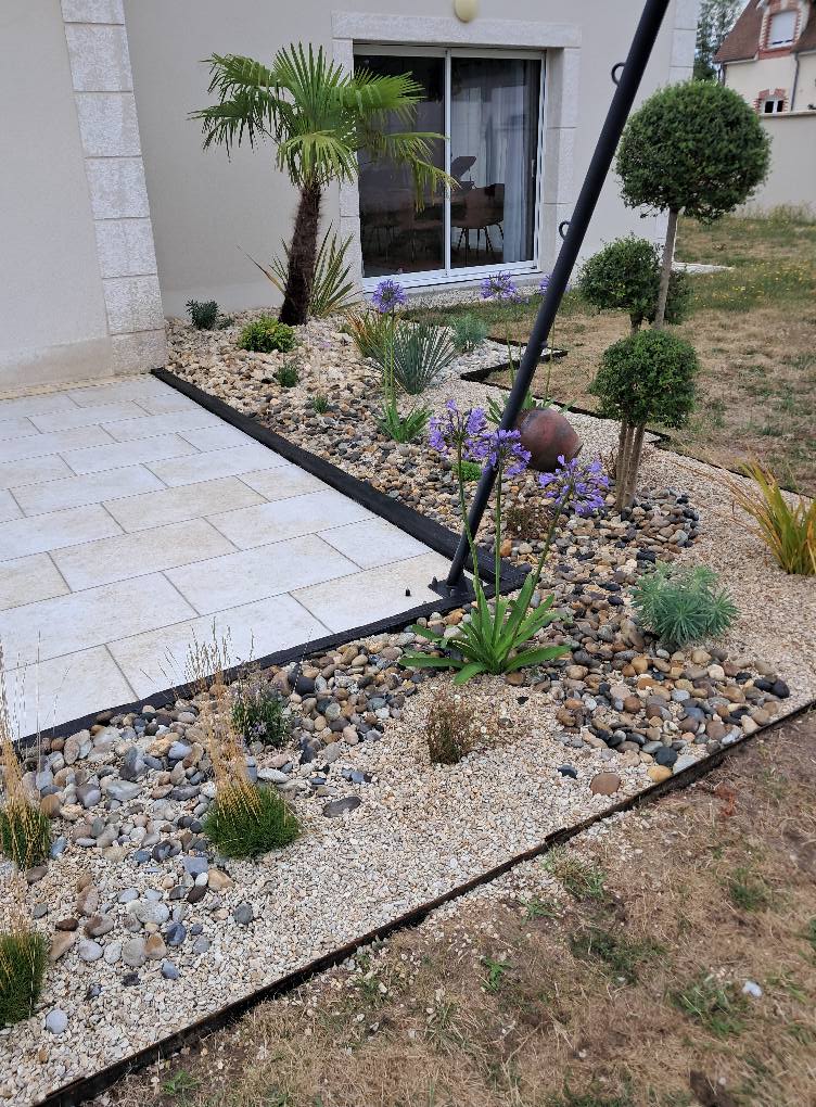 Bordure de terrasse en matériaux naturels avec graminées, buissons et fleurs violettes