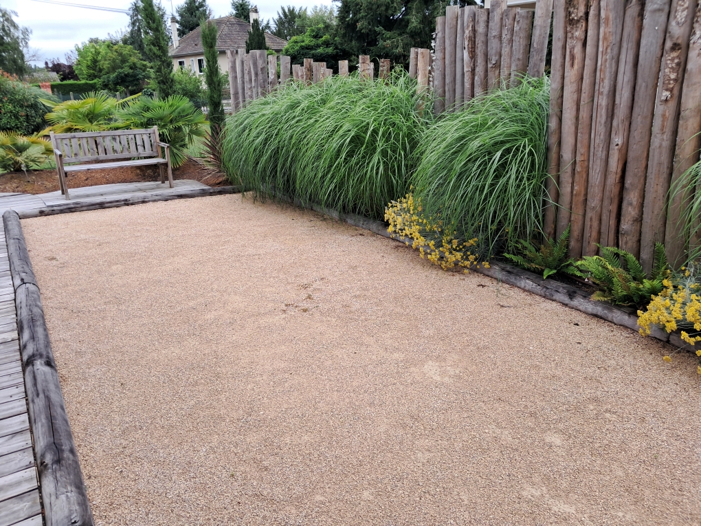 cour gravillonnée beige avec plantes vertes et clôture en bois dans le fond