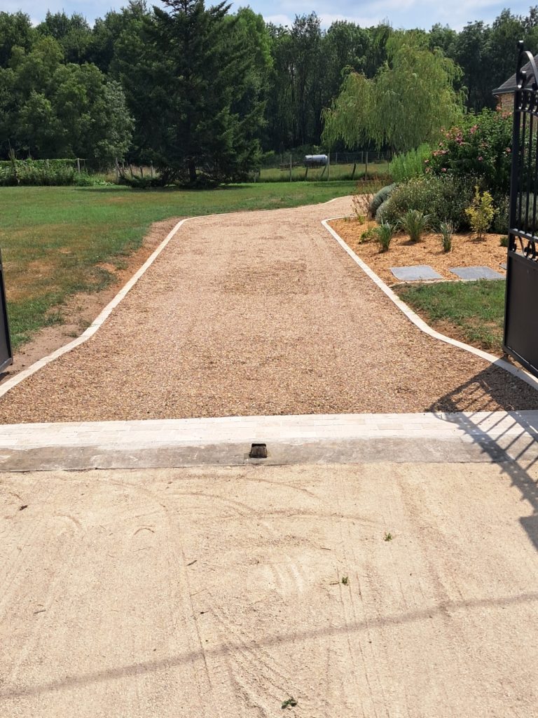 Allée en gravillons beiges, pelouse tondue de chaque côté et portail ouvert au premier plan