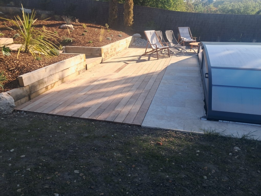 Terrasse en bois au bord d'une piscine couverte à l'extérieur avec transats dans le fond et massif à gauche